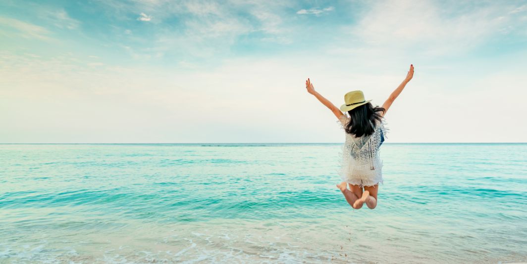 Woman jumping with arms in the air into an bright blue ocean