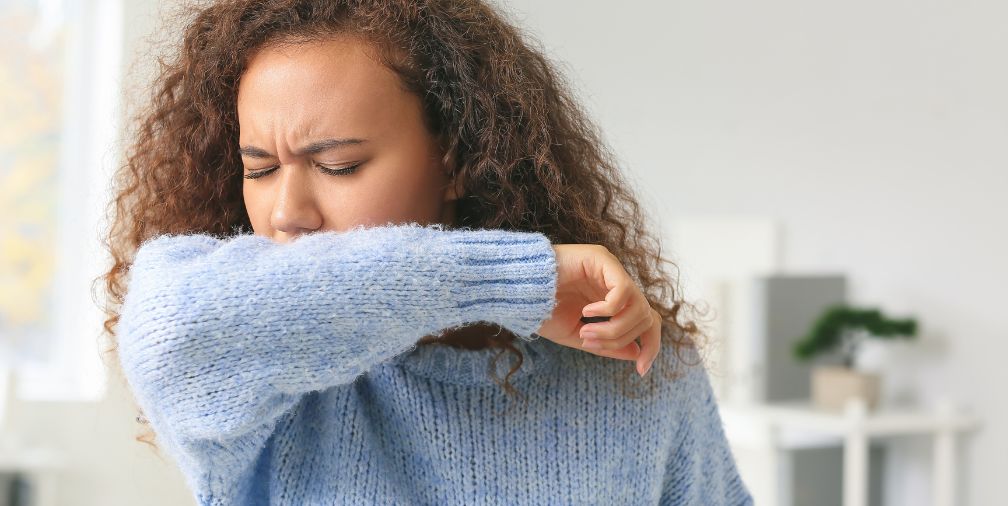 lady in blue sweater coughing into arm 