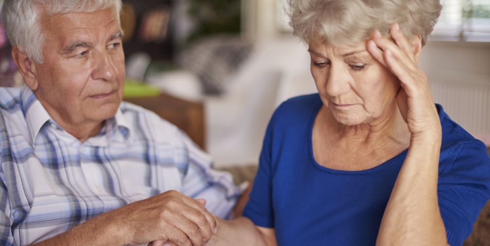 Older Couple with man holding woman's hand and woman holding her head