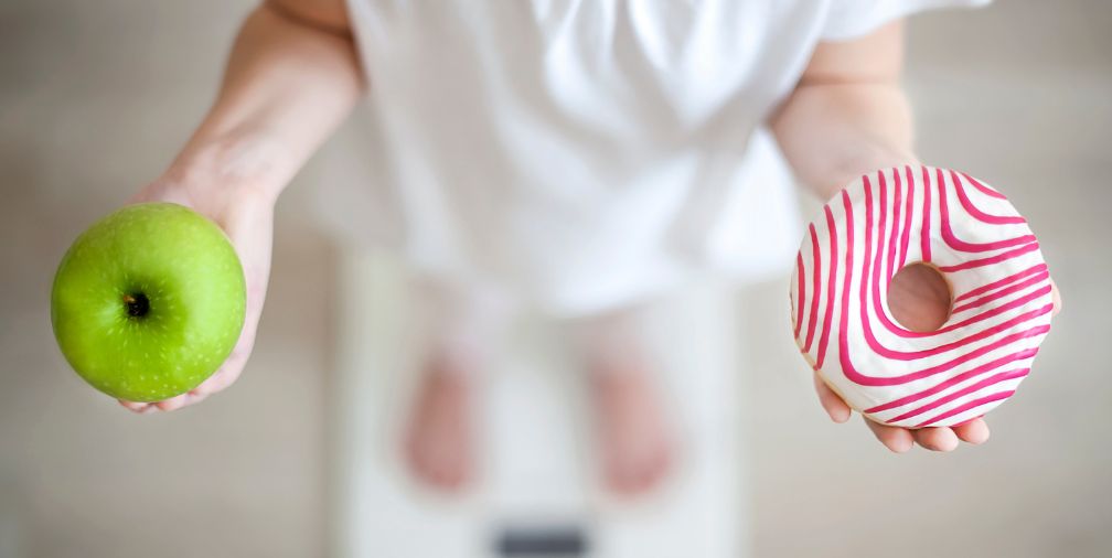 Kid in scale holding an apple and a donut 