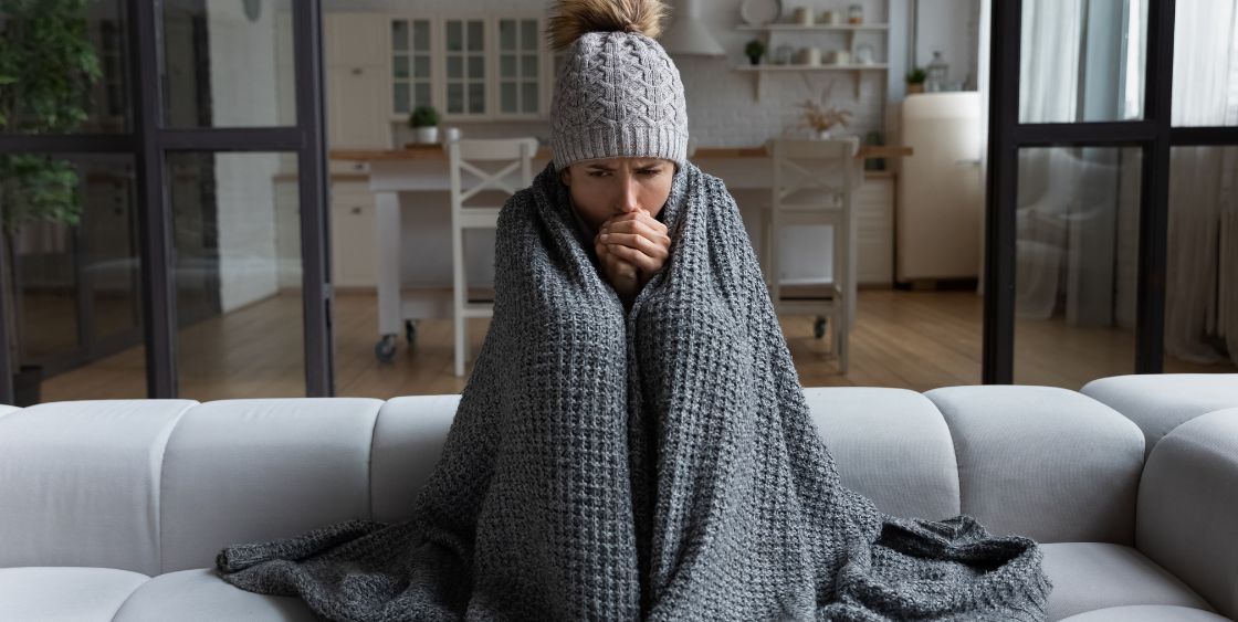 Woman on a couch bundled up with a winter hat and blanket