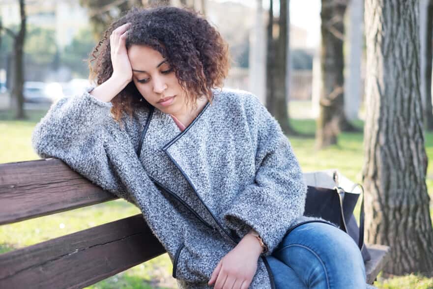 Woman sitting on a bench with hand on her head