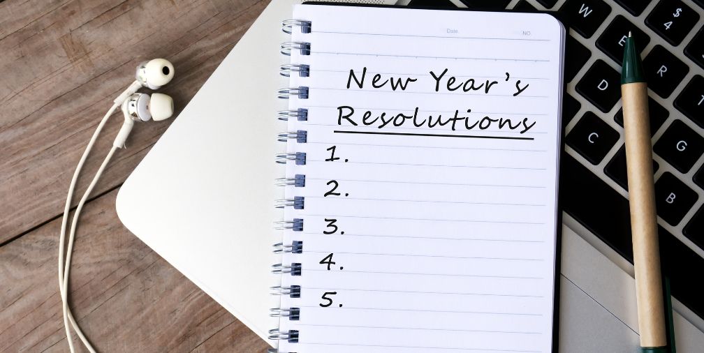 Notebook with new year's resolutions numbered 1-6 on a laptop with earbuds and a pen.